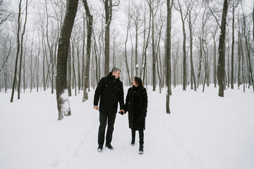 Fototapeta na wymiar A man and a woman on the background of a snow-covered forest in a snowfall