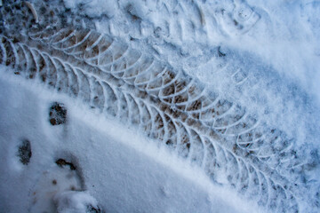 Diagonal traces of car tires in the snow on the asphalt. Close up view from above. Asphalt covered snow. Dangerous road condition. Tire trial