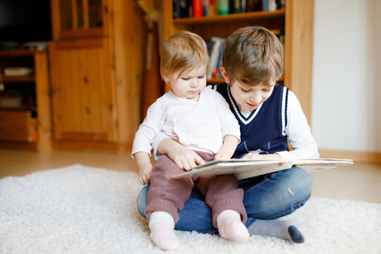 School kid boy reading book for little toddler baby girl, Two siblings sitting together and read books. Beautiful lovely family in love, cute baby and child having fun at home, indoors.