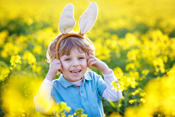 Cute little kid boy with bunny ears having fun with traditional Easter eggs hunt, outdoors....