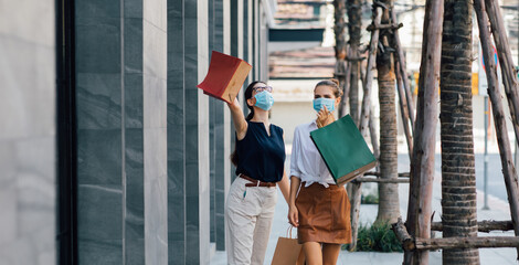 People Shopping Concept. Two beautiful caucasian woman with shopping bags walking at the mall. facemask during coronavirus and flu outbreak. Virus and illness protection