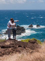 Couple embracing and overlooking the ocean from the cliffs above while the man points