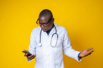 young handsome black medical doctor wearing his lab coat and hanging his stethoscope on his neck and using his smart phone