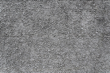 Texture of dark gray building facade cement plaster with fine gravel. Grey stone wall. Cheap finishing of facade of building with raw fine stone and plaster. Selective focus, noisy texture