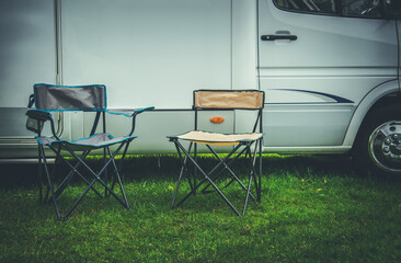 Two Empty Camping Deckchairs in Front of RV Camper