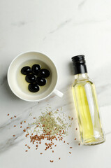 Top view of glass bottle of fresh olive oil, black olives in the cup and herbs on the marble kitchen table