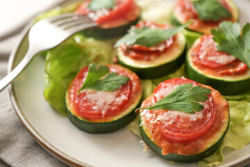 Oven baked zucchini slices as a vegetarian snack with tomato, parmesan and parsley garnish on a plate with lettuce, close-up shot