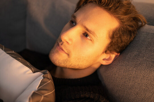  Young Attractive Man Relaxing On Couch In Living Room At Evening. Happy Man Hugging Pillow And Dreaming. 