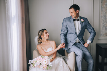 A young groom in a gray suit and a beautiful, smiling blonde bride in a white lace dress are...