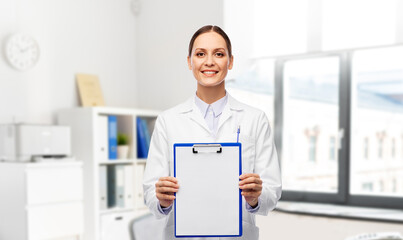 Fototapeta premium medicine, profession and healthcare concept - happy smiling female doctor in white coat showing clipboard over hospital background