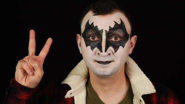 Man in demon makeup showing victory gesture on black background