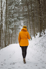 Brunette woman walks through a snowy landscape and enjoys its beauty. Girl in a yellow jacket and heels. Portrait of confident sportswoman in antique white tone. 20-24 years. Walk through forest