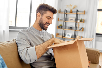 mail delivery, shipment and people concept - happy smiling man opening parcel box at home