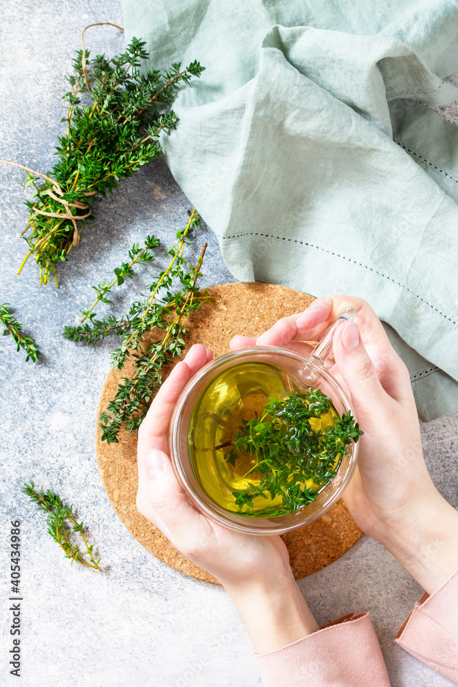 Wall mural Therapeutic herbal tea. Woman holds a hot cup of thyme tea. Top view flat lay.