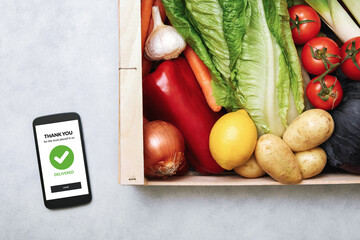 Fresh food delivery service concept. Top view of a smartphone and wooden box full of fresh vegetables at home. Grocery online order.