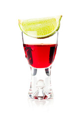 Shot of red liquid with a lime clove over, served in a transparent glass. Studio photo isolated on white background.