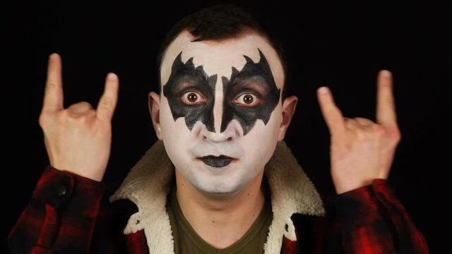 Man in demon makeup showing rock and roll sign, devil horns gesture and looking with crazy expression