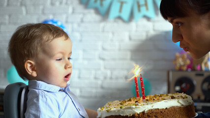 Mother helping her little son blowing out candle on a birthday cake