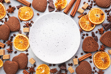 Chocolate heart cookies, oranges cinnamon and spicy spices on a gray table, top view, copy space.