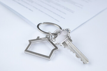 Close-up of a key with a keychain in the shape of a house, documents in the background. The concept of buying and insuring real estate, apartments, mortgages. Light colors, copy space.