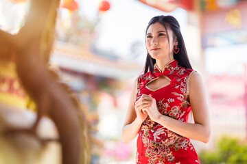 beautiful Asian young woman wearing red traditional Chinese cheongsam decoration Stand for pray to buddha statue for Chinese New Year Festival at Chinese shrine in Thailand