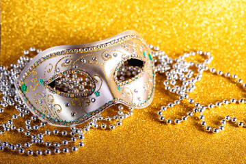 Festive, colorful Mardi Gras or carnivale mask and beads on golden background. Venetian masks....