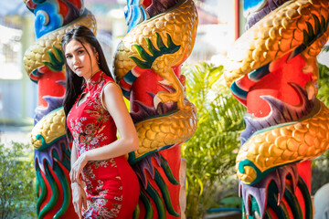 Portrait beautiful smiles Asian young woman wearing red traditional Chinese cheongsam decoration for Chinese New Year Festival at Chinese shrine in Thailand
