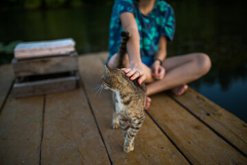 Fototapeta na wymiar a girl sits on a wooden pier and watches a cat walking on the boards