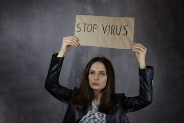 young attractive girl holds a Stop virus poster on a gray background