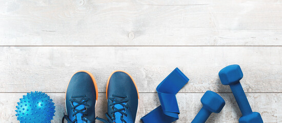 Healthy lifestyle blue and red gender neutral sports accessories grouped with shoes on white wood. Fitness and home or gym exercise monochrome items banner with copy space. Workout
