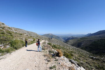 Obraz premium Woman and child hiking on mountain track in the Vall de Laguart, Benimaurell, Alicante Province, Valencia, Spain. In the distance is Montgo mountain, the coast and the Mediterranean Sea