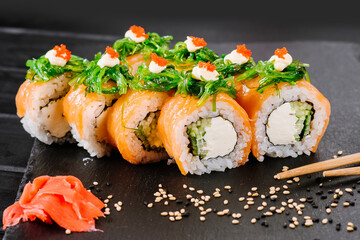 Tasty sushi rolls with salmon and chuka on black background