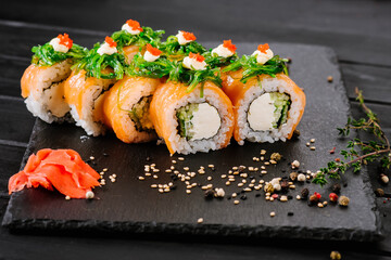 Tasty sushi rolls with salmon and chuka on black background