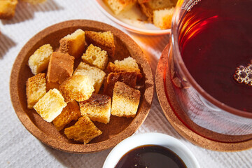 Square toasted pieces of homemade delicious rusk, hardtack, Dryasdust, zwieback, Liquid honey in a saucer and black tee in a cap on a white tablecloth.