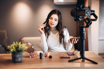 Beauty blogger nice female filming daily make-up routine tutorial on camera. Influencer young woman live streaming cosmetics product review in home studio. Vlogger job. DIY putting makeup