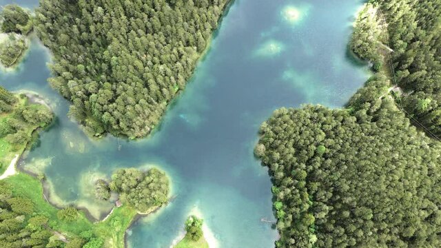 ein alpen see mit einer bewaldeten insel umgeben von blau t&uuml;rkisen wasser von oben betrachtet