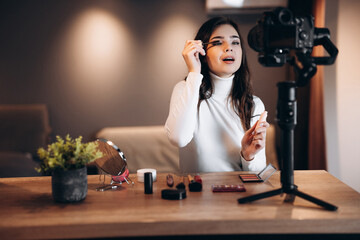Beauty blogger pretty female filming daily make-up routine tutorial on camera. Influencer young woman live streaming cosmetics product review in home studio. Vlogger job. DIY.