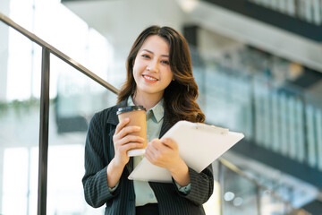 Young Asian businesswoman standing holding documents and coffee cup