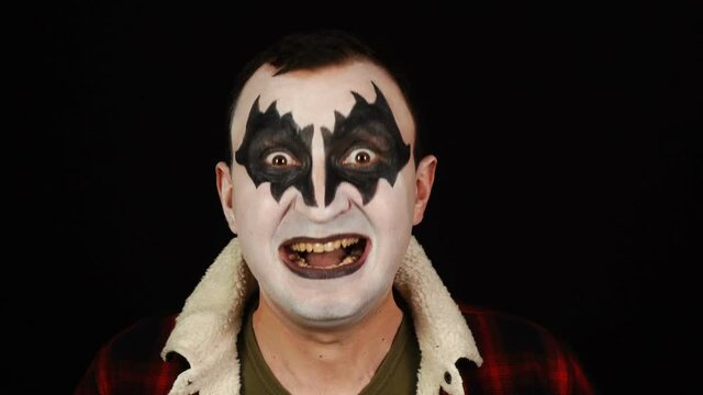 Man in demon makeup shouts loudly with his mouth wide open on black background