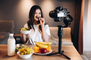 Healthy food blogger young female eating fresh vegan salad in kitchen studio, filming tutorial on...