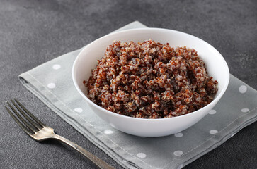 Cooked red quinoa in a white plate on a gray background. Close-up