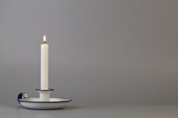 White candle in an old white candlestick on a gray background close-up.
