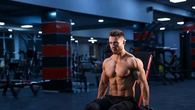 Handsome power athletic man bodybuilder doing exercises with dumbbells. Fitness muscular body on dark gym background.