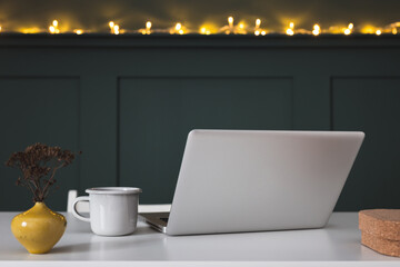 Home office desk with dark wall, plant, laptop and cup. Minimalist workspace.