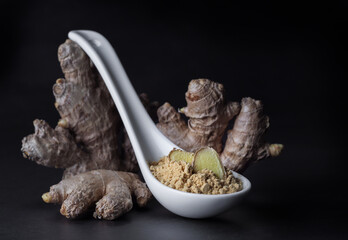 Ginger root and ginger powder in a spoon isolated at black background, close-up.