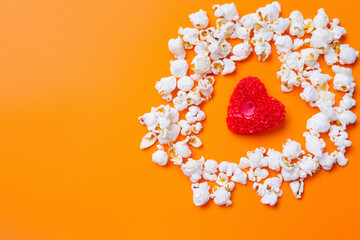  Popcorn and a candle in the shape of a red heart on orange background with blank space.