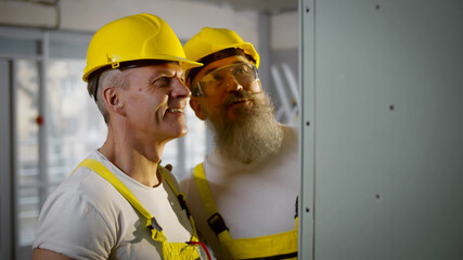 Builder and foreman in safety uniform examining drywall at construction site