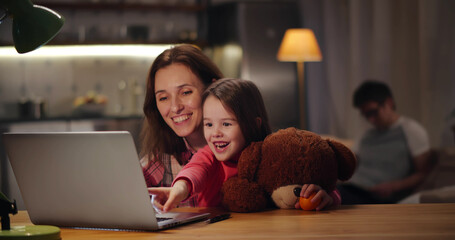Happy mother and little daughter at home working on computer together