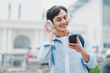The man is wearing a backpack, listening to music and using the phone