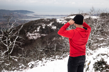 Young man at the top of a snowy mountain with a red sweater and black jeans.